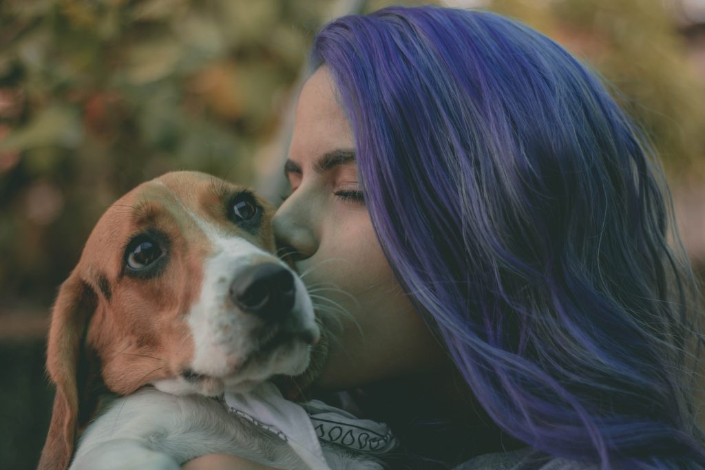 Ragazza coi capelli viola bacia un cane beagle sulla guancia. Il cane ha lo sguardo perplesso
